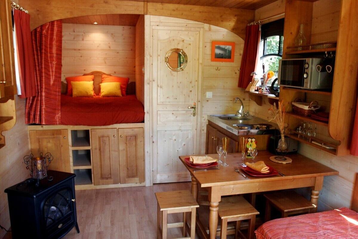 A cozy cabin with a bed, a small kitchenette, a dining table, and a wood-burning stove.