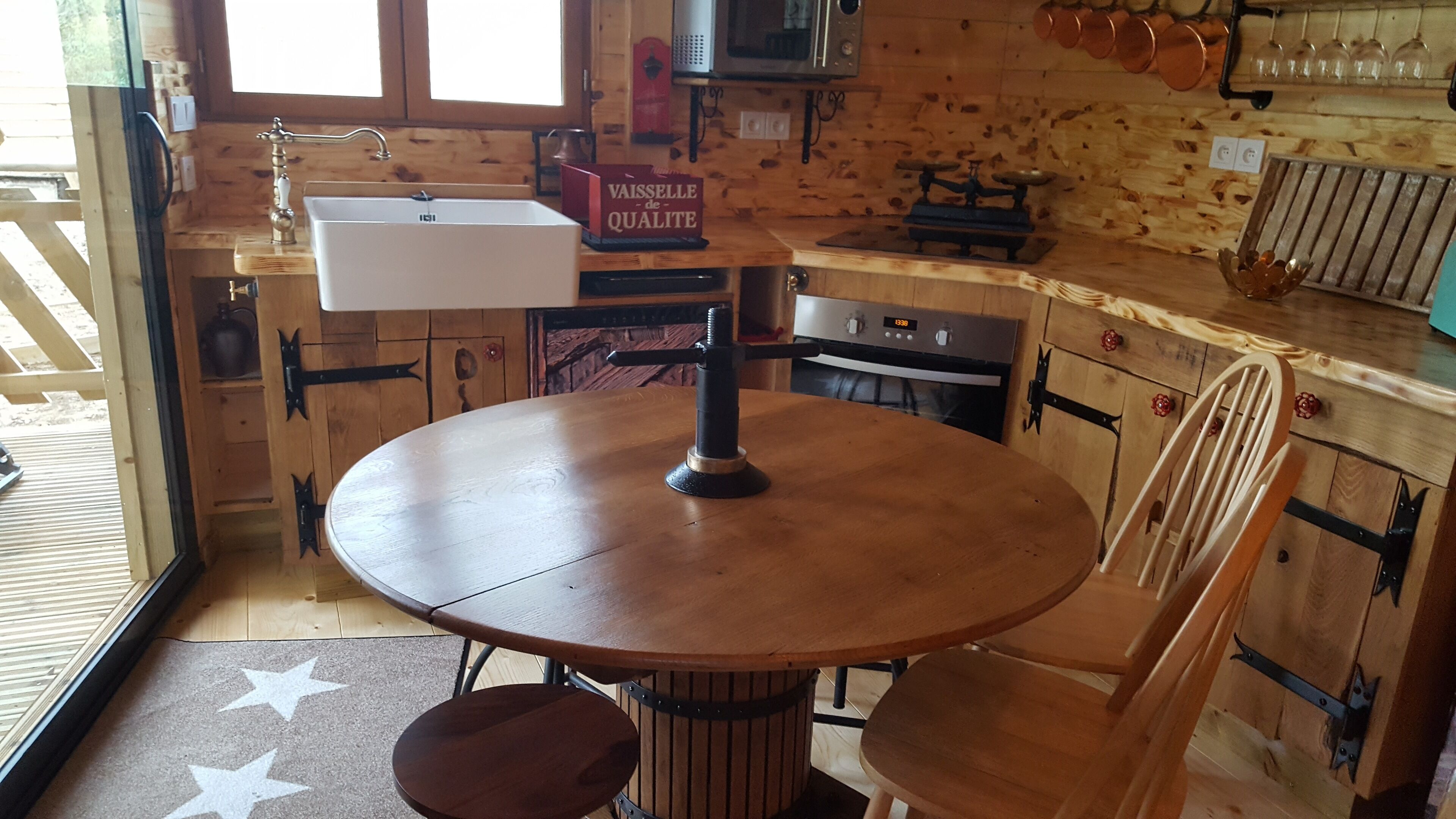 A wooden interior with a round table, a chair, a sink, and a vintage scale.