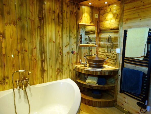 A wooden cabin bathroom with a freestanding bathtub, a wooden sink basin, and a towel rack.