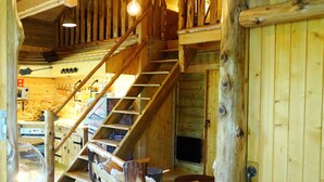 Un intérieur en bois avec un escalier, des poutres apparentes et des luminaires suspendus.