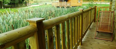 A wooden deck with a railing overlooking a field of tall grass and a wooden cabin in the background.