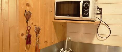 A kitchen with wooden walls, a stainless steel sink, a microwave, and various utensils hanging on the wall.