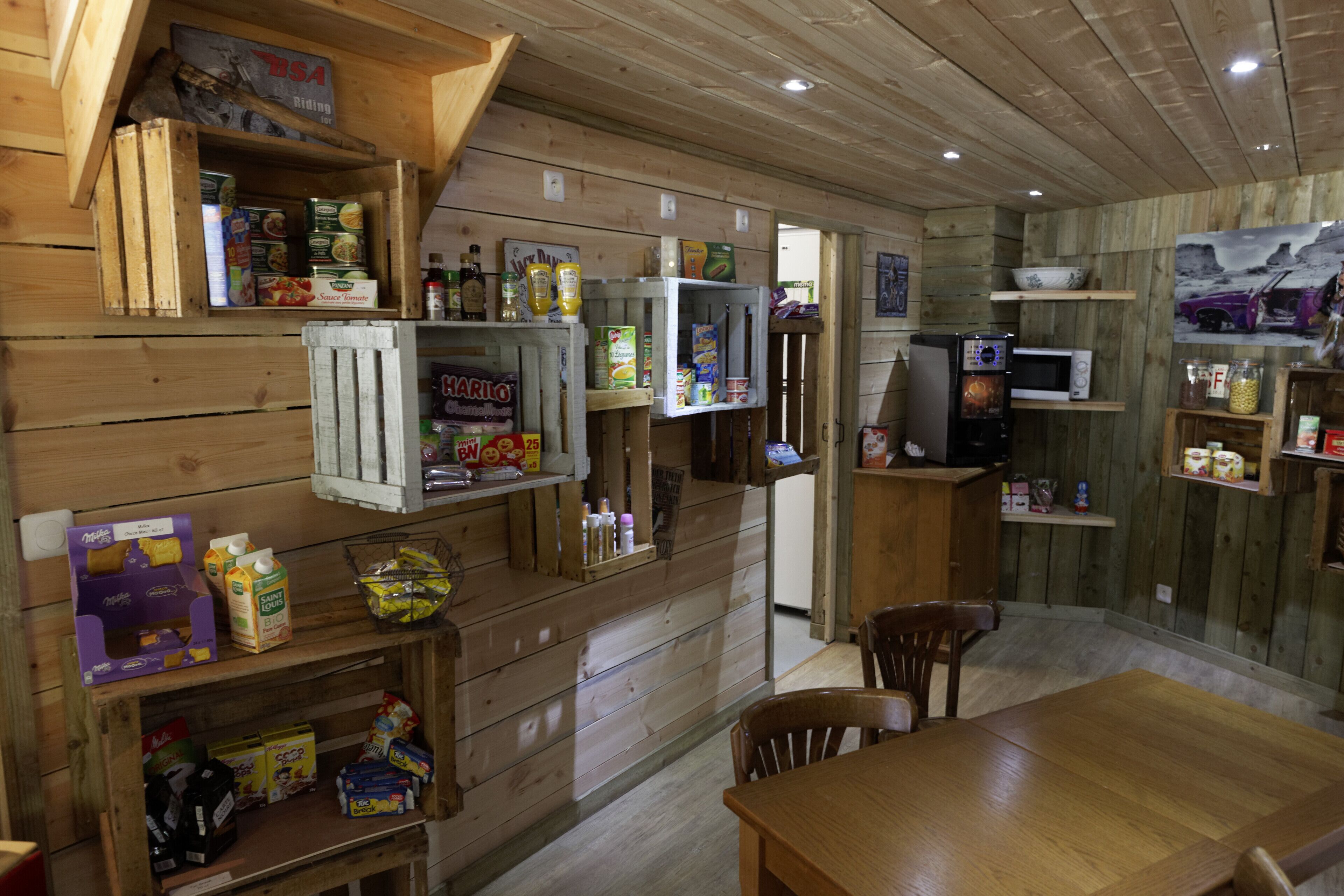 A rustic wooden interior with shelves stocked with snacks, a microwave, and a dining area with chairs.