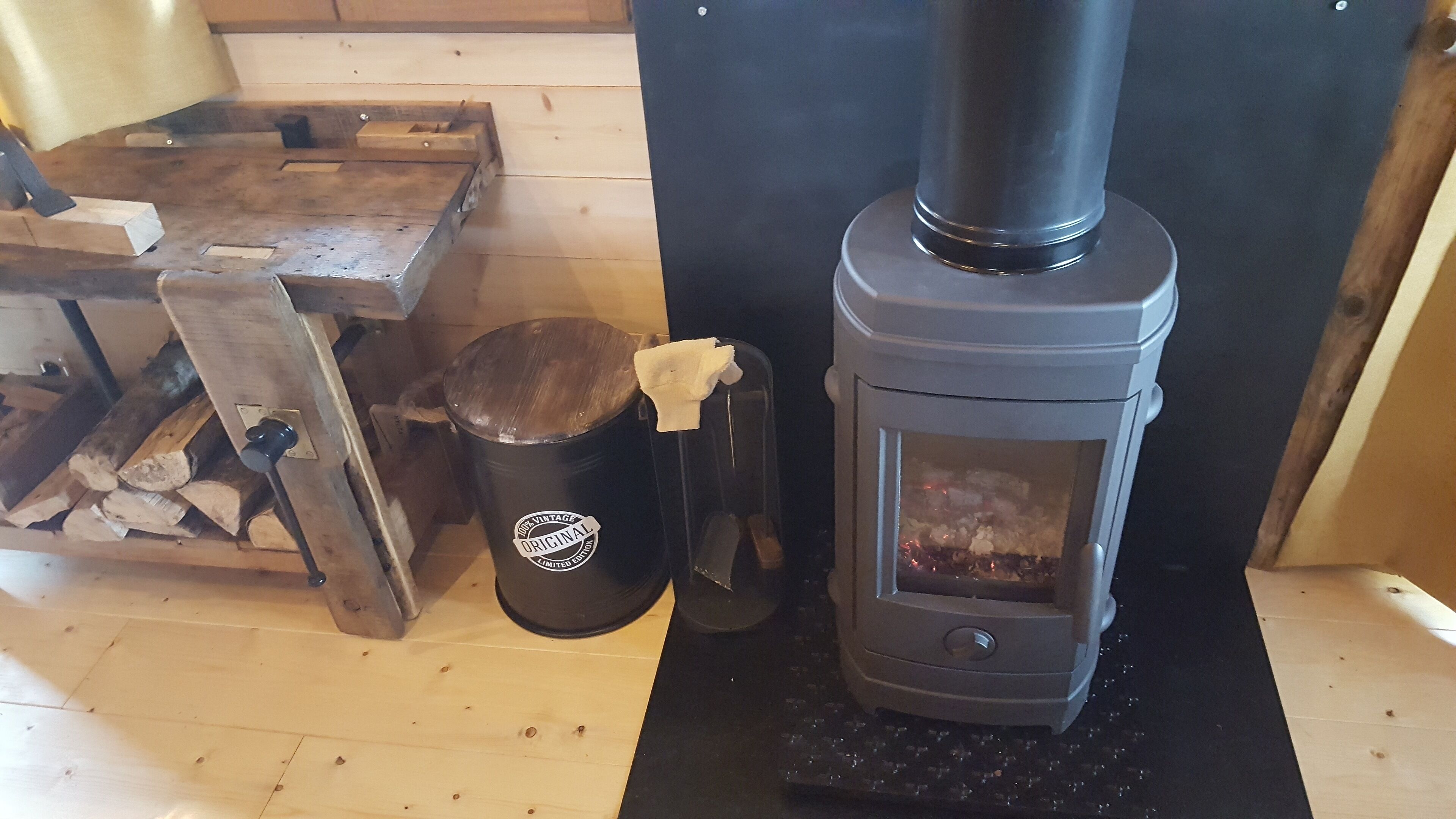 En vedkamin med en metalldörr, en soptunna och ett träbord med vedstaplar.