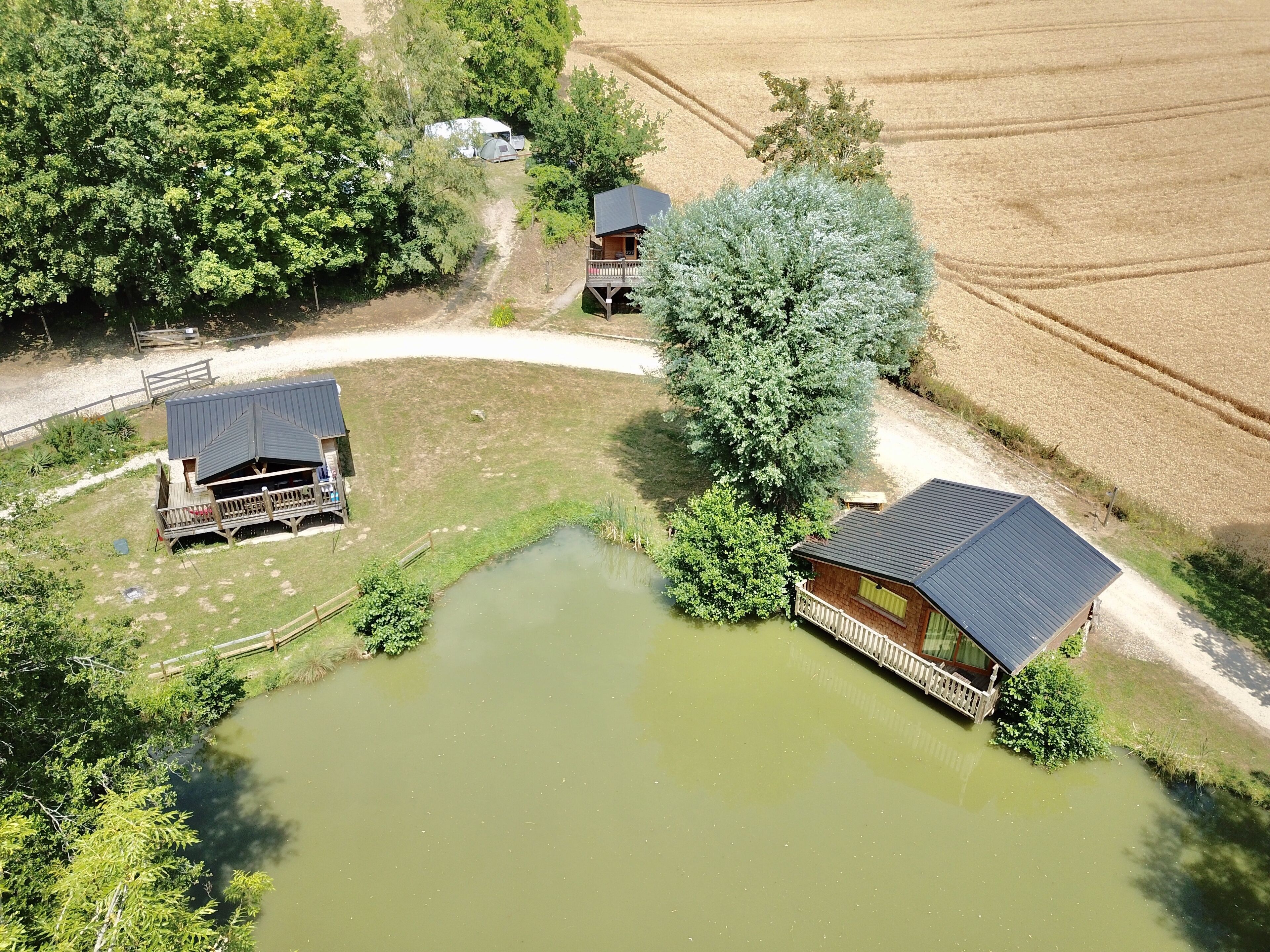 Una propiedad rural con un estanque, una cabaña de madera y una casa más grande con porche.
