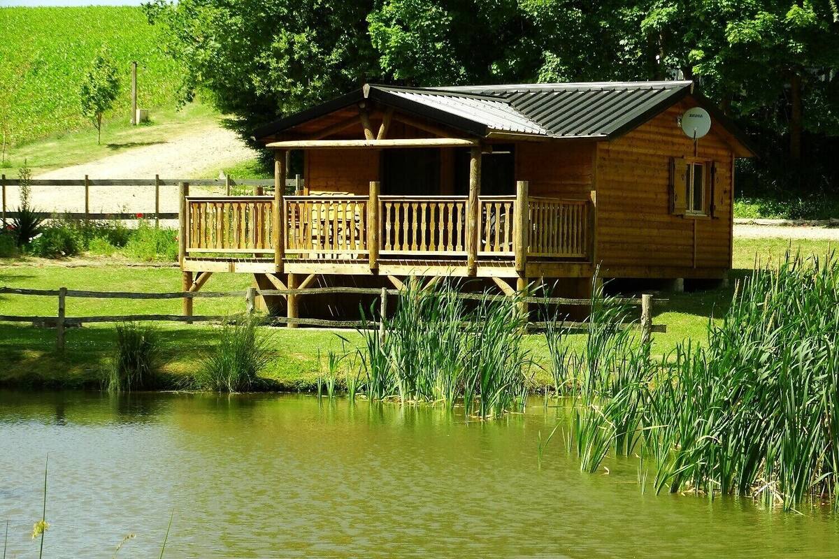 A wooden cabin with a balcony, situated by a pond with tall grasses.