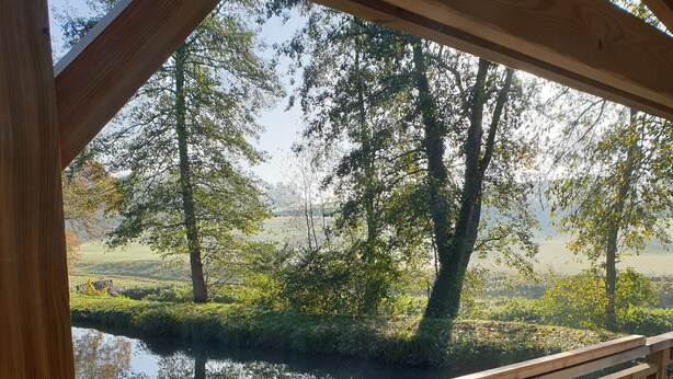 Une terrasse en bois avec une balustrade en treillis, donnant sur une étendue d’eau calme et des arbres.