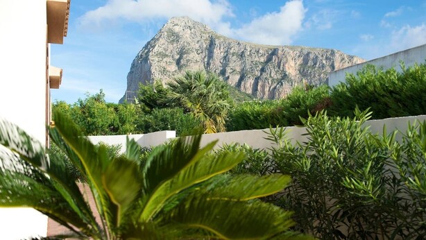 Un patio rodeado de vegetación y paredes blancas, con una montaña al fondo.
