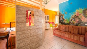 Una habitación con techo de madera, una zona de comedor con una mesa y sillas, un sofá y un mural grande con una escena submarina.