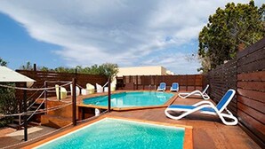Una piscina rectangular con dos sillas de descanso y una terraza de madera.