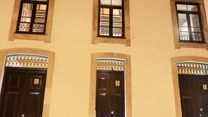 A building with three black doors and windows with metal grilles, set against a plain wall under a dark sky. - National Theater House 24 (Porto)