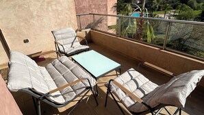 Un balcon avec deux fauteuils confortables et une petite table, donnant sur une piscine et un espace verdoyant.