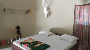 Un dormitorio con cama, una silla, mosquitera y cortina.