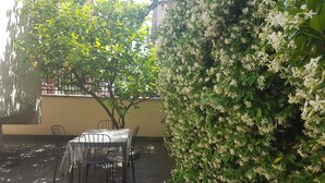 Ein Sitzbereich im Freien mit Tisch und Stühlen, umgeben von üppigem Grün und blühenden Pflanzen.