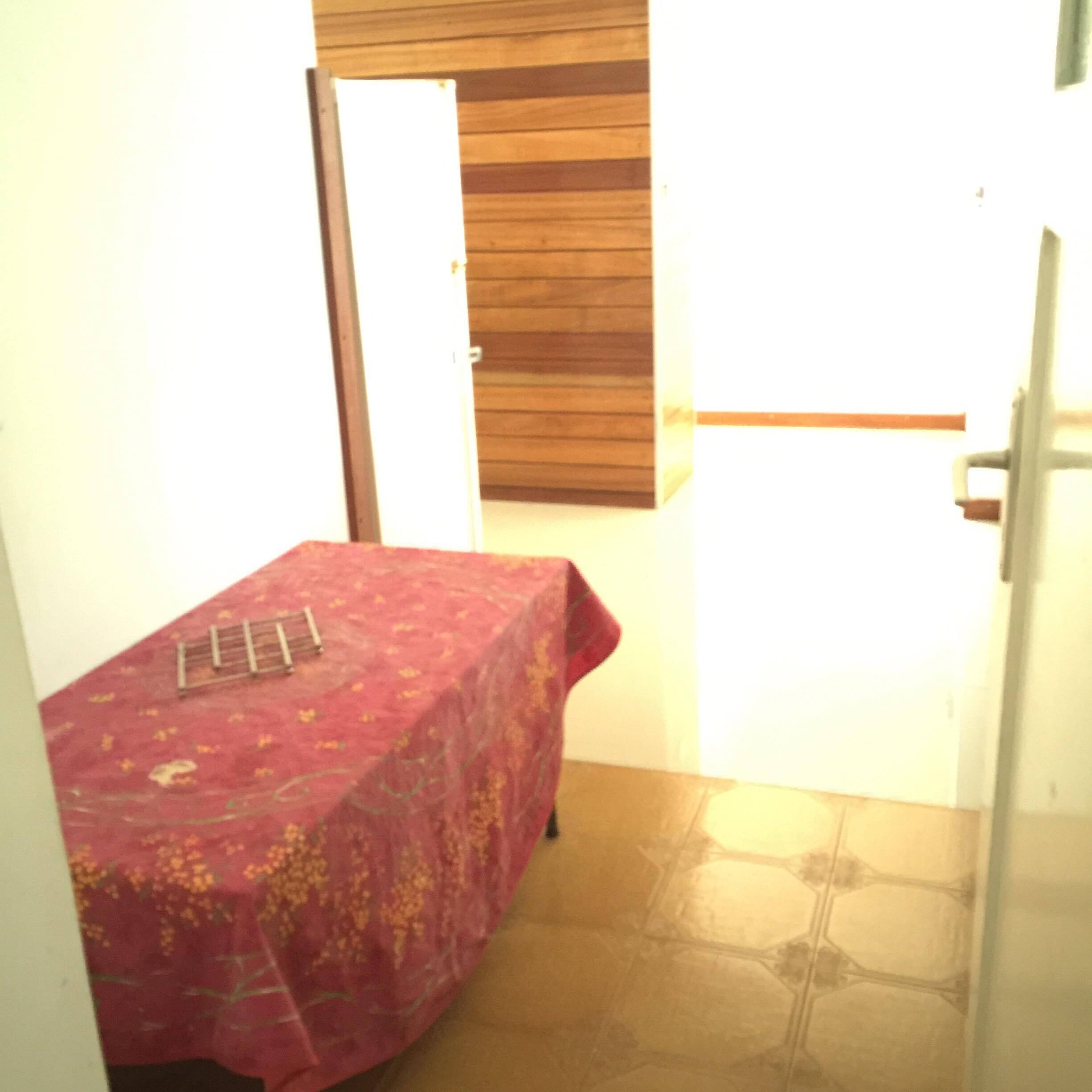 Ein kleines Zimmer mit einem Bett, das mit einem roten, floralen Bettbezug bezogen ist, einer Holzhackenwand und einem gefliesten Boden.