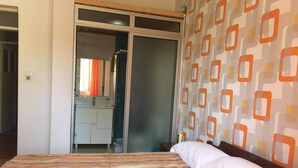 A bedroom with a bed, a wardrobe, and a bathroom visible through an open door. - Nossa Casa Vossa Casa (Tarrafal)