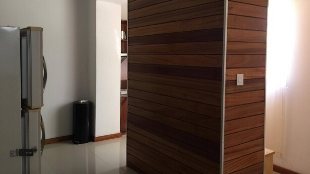 A room with a wooden partition, a refrigerator, a trash bin, and a door leading to another room. - Nossa Casa Vossa Casa (Tarrafal)