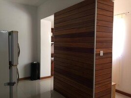 Una habitación con separador de madera, refrigerador, cesto de basura y una puerta que da a otra habitación.
