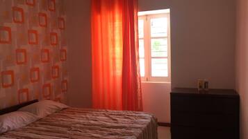 A bedroom with a bed, a window with curtains, a dresser, and a patterned wall.
