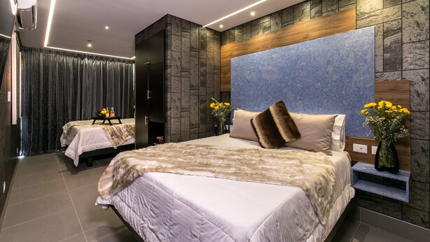 A modern hotel room with two beds, a large stone accent wall, a wooden headboard, and a small bedside table with a vase of flowers. - 2 Luxury Rooms With Window (Medellín)