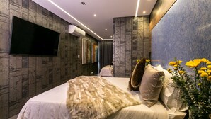 A modern hotel room with a large bed, a flat-screen TV mounted on the wall, and a decorative vase with flowers on the nightstand. - 2 Luxury Rooms With Window (Medellín)