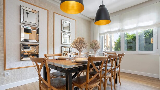 A dining area with a black table, wooden chairs, and a black and gold pendant light.