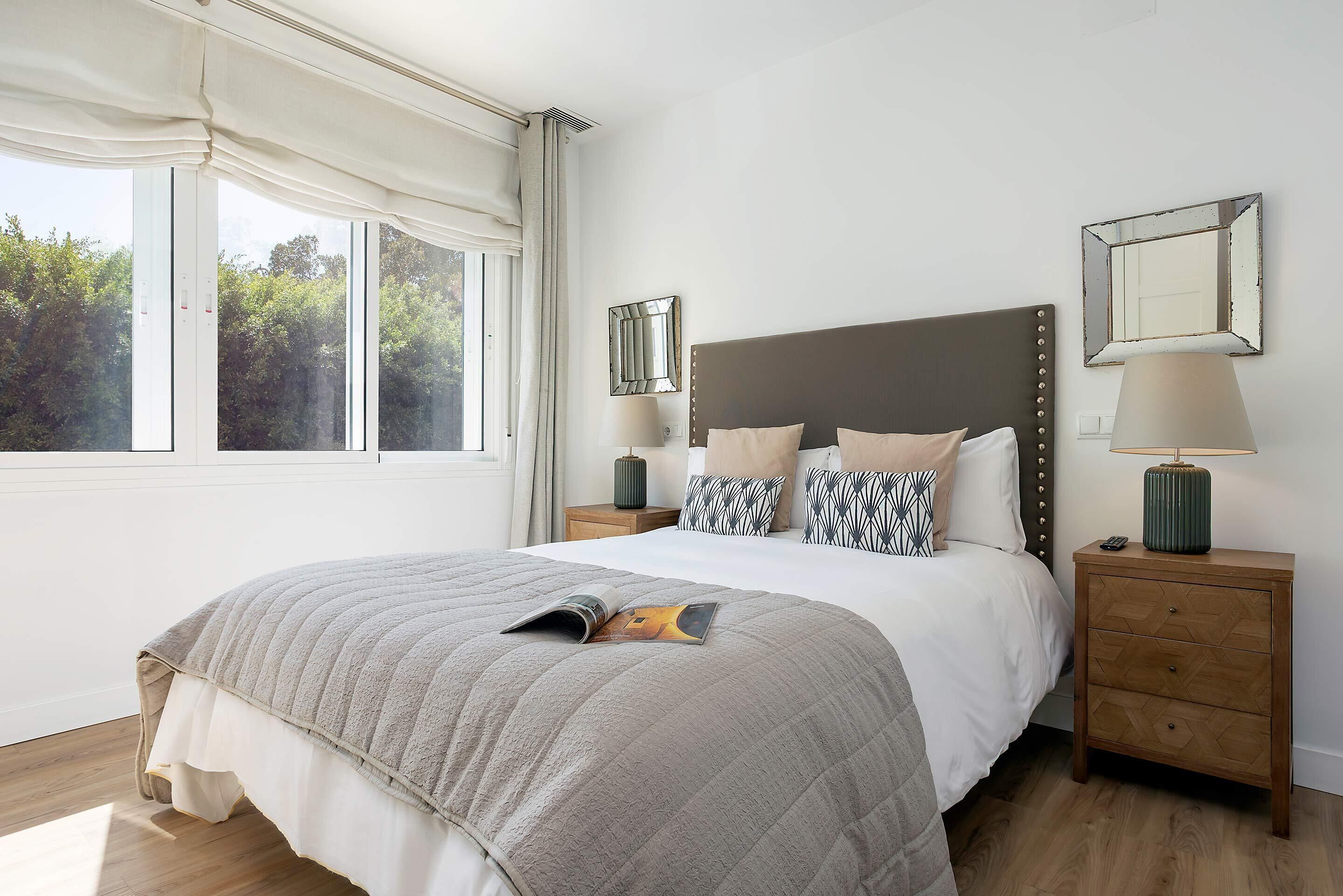 A bedroom with a bed, bedside tables, a window, and a view of trees.