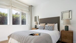 A bedroom with a bed, bedside tables, a window, and a view of trees.