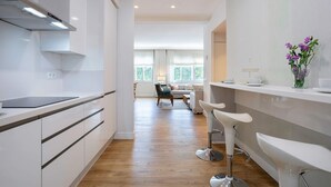 A modern kitchen with white cabinetry, a stainless steel range hood, and a bar area with white bar stools.