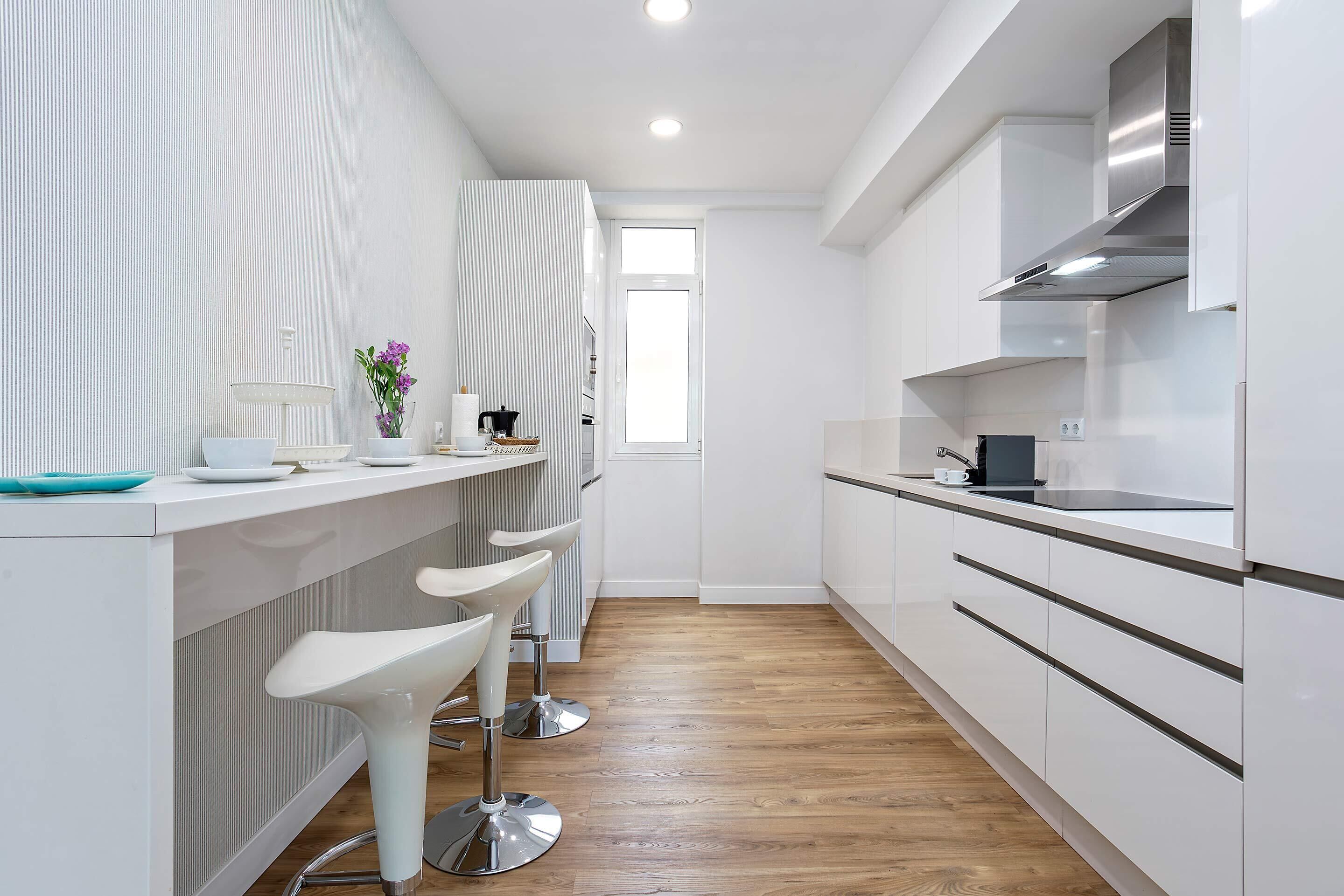 A modern kitchen with white cabinetry, a stainless steel range hood, and a window providing natural light.