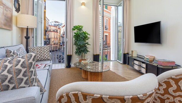 Ein modernes Wohnzimmer mit Sofa, Couchtisch, Fernseher und einem Balkon mit Blick auf die Stadt.