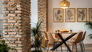 Et spiseområde med en murstenssøjle, moderne stole, et glasbord og indrammede botaniske tryk på væggen.