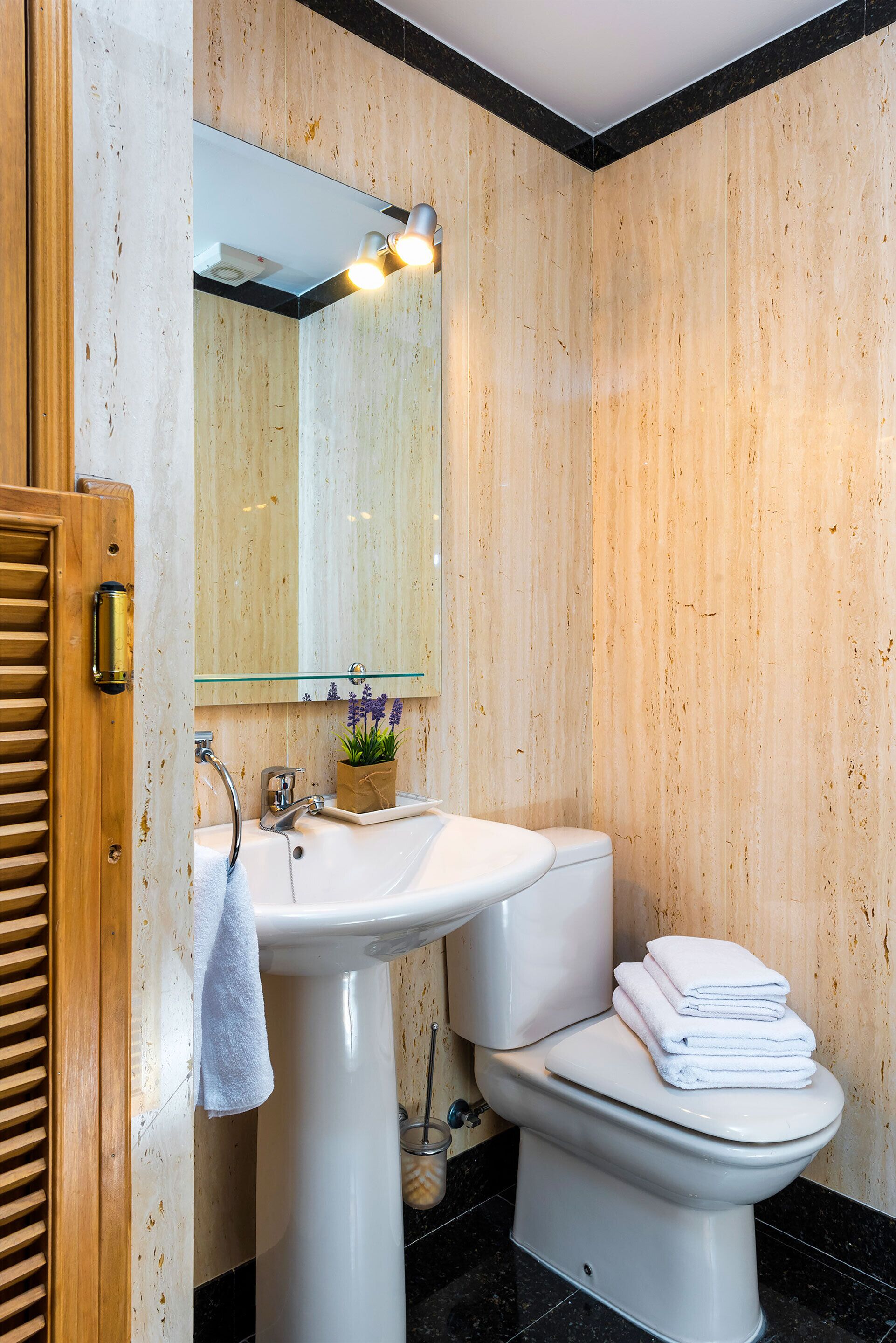 Une salle de bain avec un mur en bois, un lavabo blanc, des toilettes et un miroir avec des lumières.