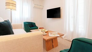 A modern hotel room with a wooden coffee table, a flat-screen TV mounted on the wall, and a green armchair. - Genteel Home Velarde (Seville)