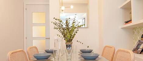 A dining area with a glass table, wicker chairs, and a vase with green foliage.