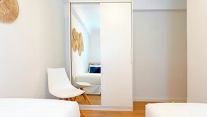 A modern bedroom with two beds, a white chair, and a wardrobe. - Genteel Home Velarde (Seville)