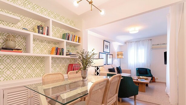 A modern living room with a glass dining table, wicker chairs, a bookshelf, a green armchair, and a lamp. - Genteel Home Velarde (Seville)