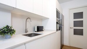 A modern kitchen with white cabinetry, a stainless steel sink, a microwave, and a toaster. - Genteel Home Velarde (Seville)