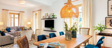 Uma sala de estar moderna com área de jantar, destacando uma grande mesa de madeira, cadeiras azuis, uma cadeira de vime e um pendente de rattan.