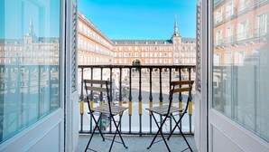 A balcony with two wooden chairs and a metal railing, overlooking a historic square with ornate buildings and a prominent tower. - Apartment 1Bd With Balcony in Plaza Mayor Square. Plaza Mayor III (Madrid)