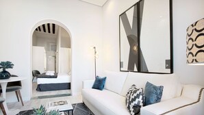 A modern living room with a white sofa, a coffee table with plants, a dining area with a white table and chairs, and a hallway leading to a bathroom. - Apartment 1Bd With Balcony in Plaza Mayor Square. Plaza Mayor III (Madrid)