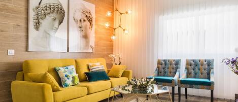 A modern living room with a yellow sofa, two armchairs, a glass coffee table, and a decorative light fixture.