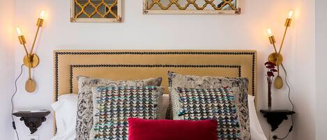 A bedroom with a bed, patterned pillows, a red throw, and wall-mounted sconces.