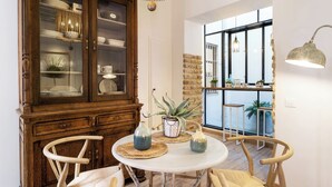 A dining area with a round table, wooden chairs, a cabinet with glass doors, and a view through a large window.