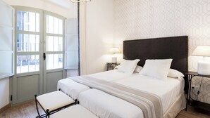 A hotel room with a large bed, two bedside tables with lamps, a window with curtains, and a geometric patterned wall.