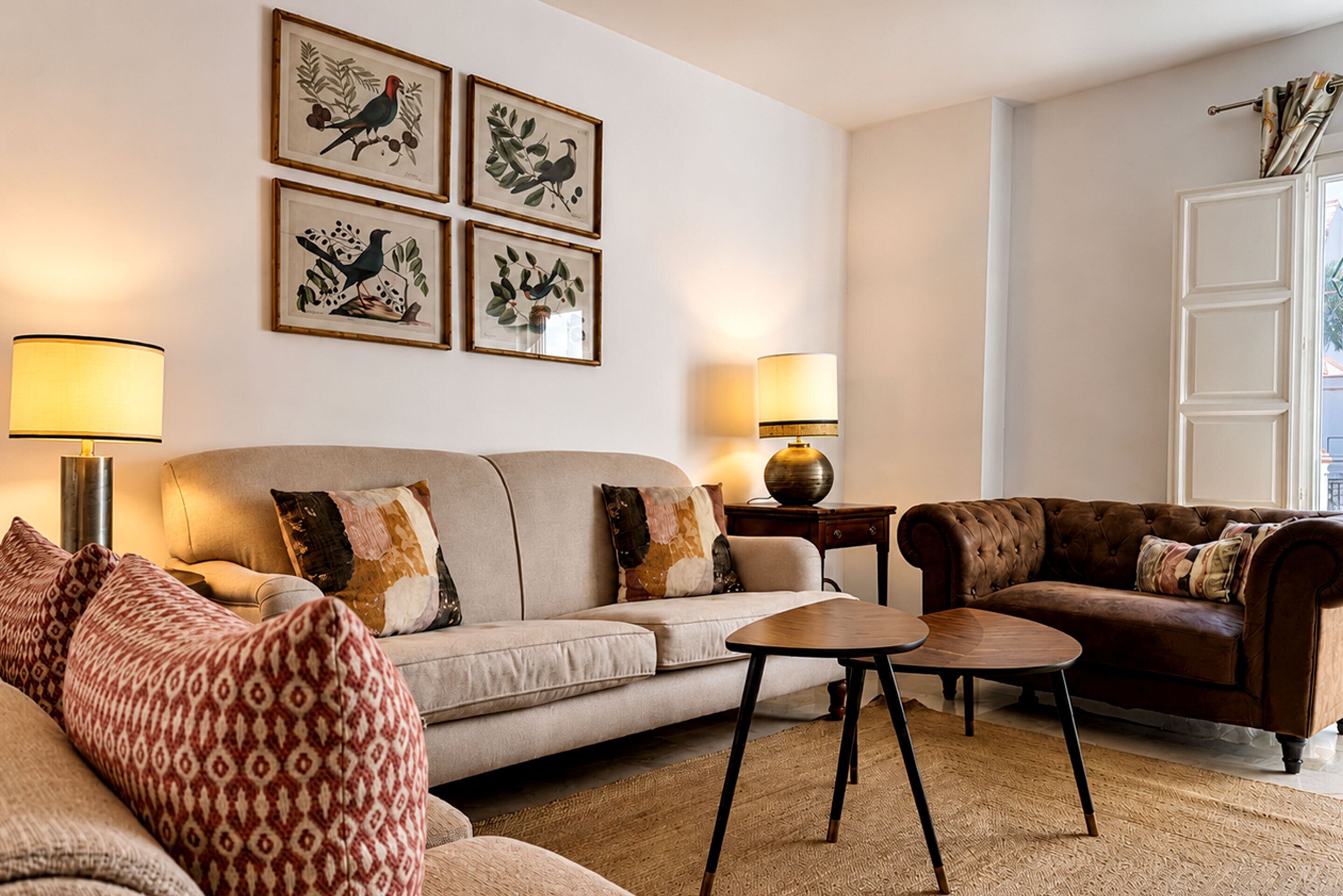 A living room with a sofa, two armchairs, a coffee table, and a side table with lamps. There are four framed pictures on the wall.