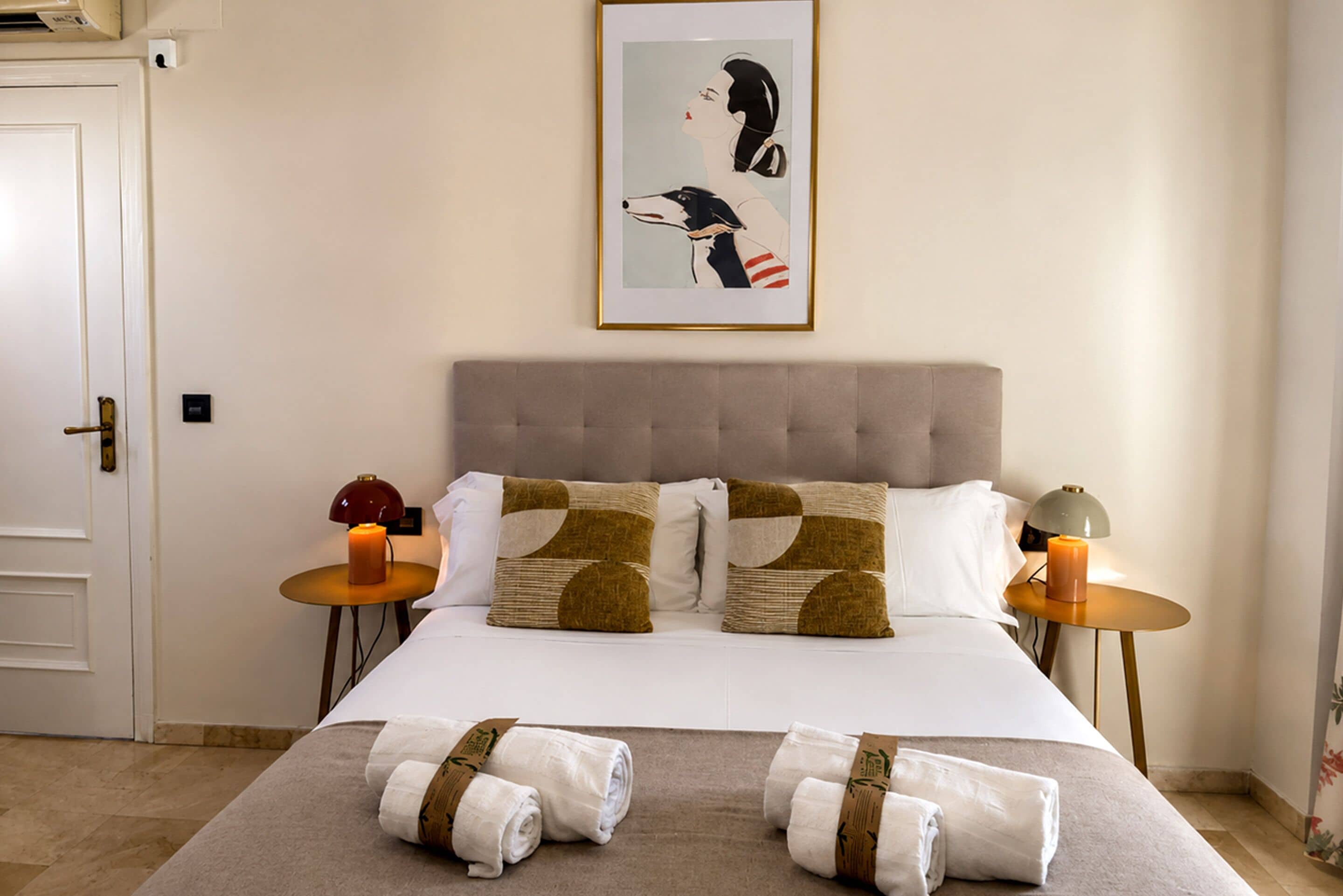 A hotel room with a bed, two nightstands, a framed artwork, and rolled towels.