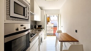 A modern kitchen with built-in appliances, a dining area with a wooden table and chairs, and a view of a red balcony.