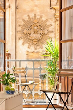 A balcony with a wrought iron railing, a small table with a plant, a glass of water, and a metal chair. - Genteel Home Sagrado Corazón (Granada)