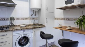 A compact kitchen with a washing machine, a microwave, a sink, and two bar stools. - Genteel Home Reyes Católicos (Granada)